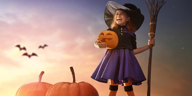 Girl wearing a halloween costume holding a carved pumpkin